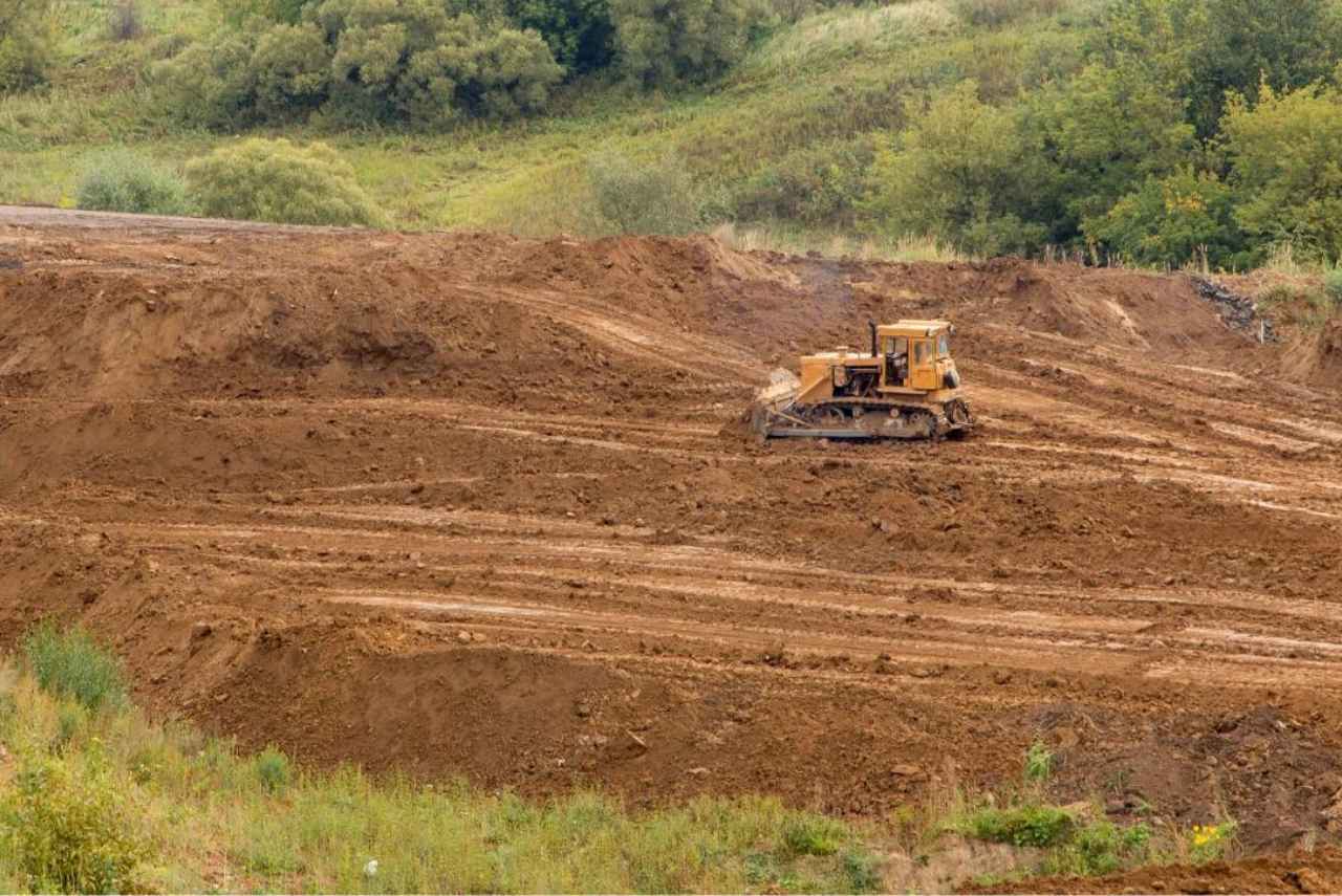 A tractor is driving through the dirt on a hill.